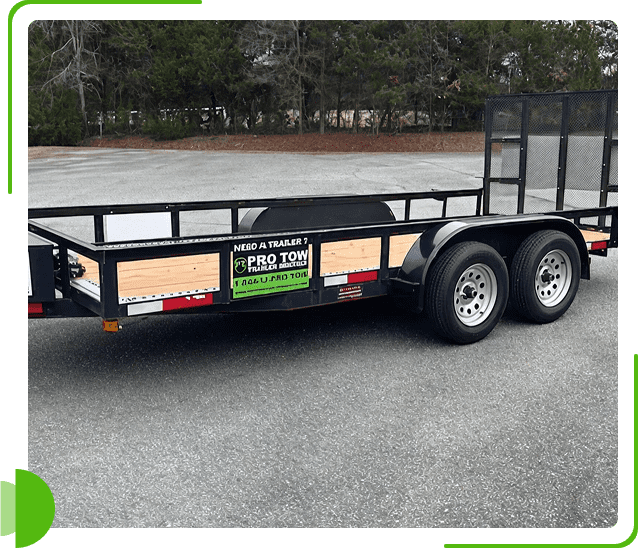 Black utility trailer parked on asphalt with trees in background.